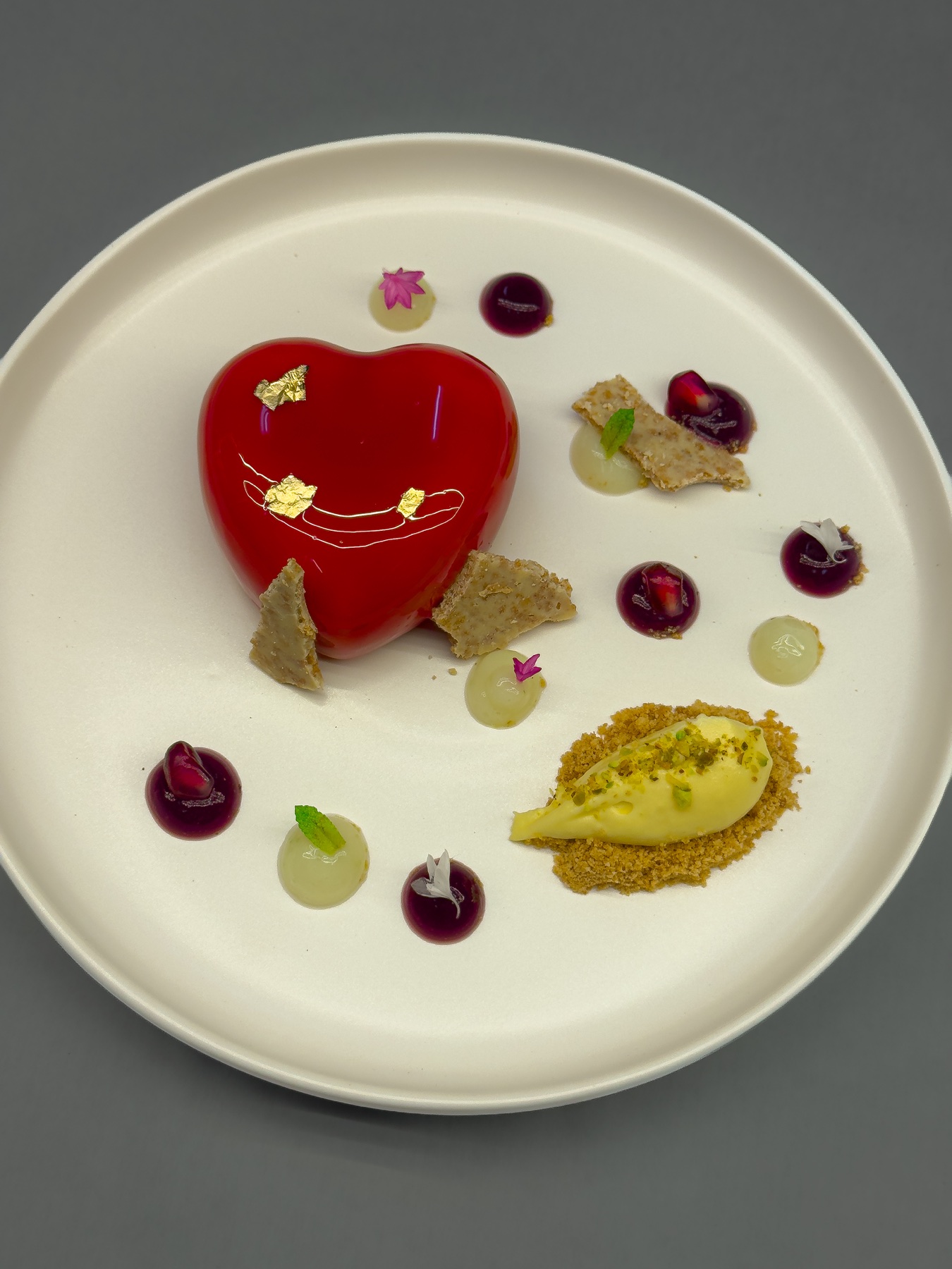 A polished red dessert with fruit, gold leaf, and frozen elements