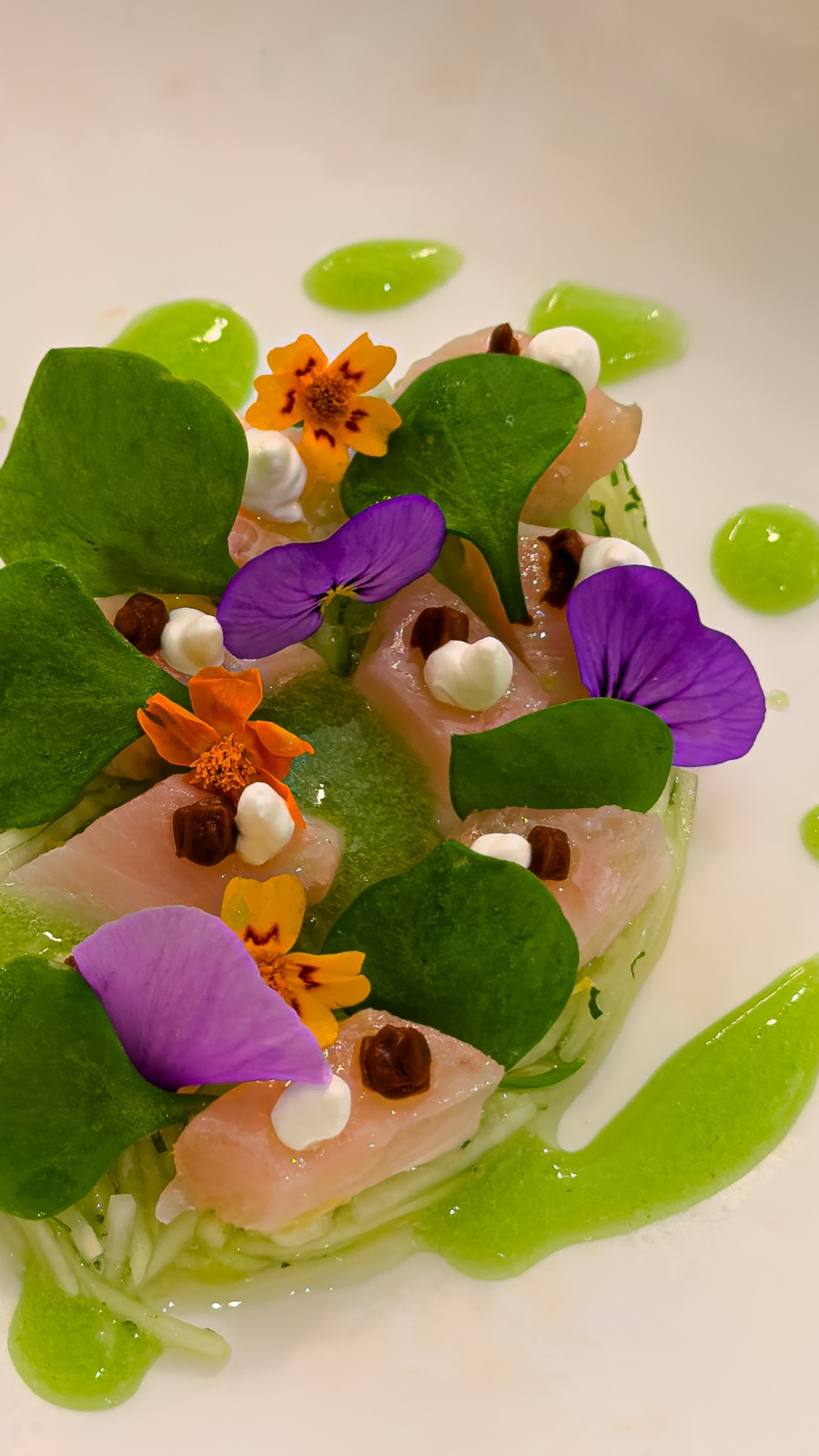 A refined plate with herbs, edible flowers, and bright green sauce